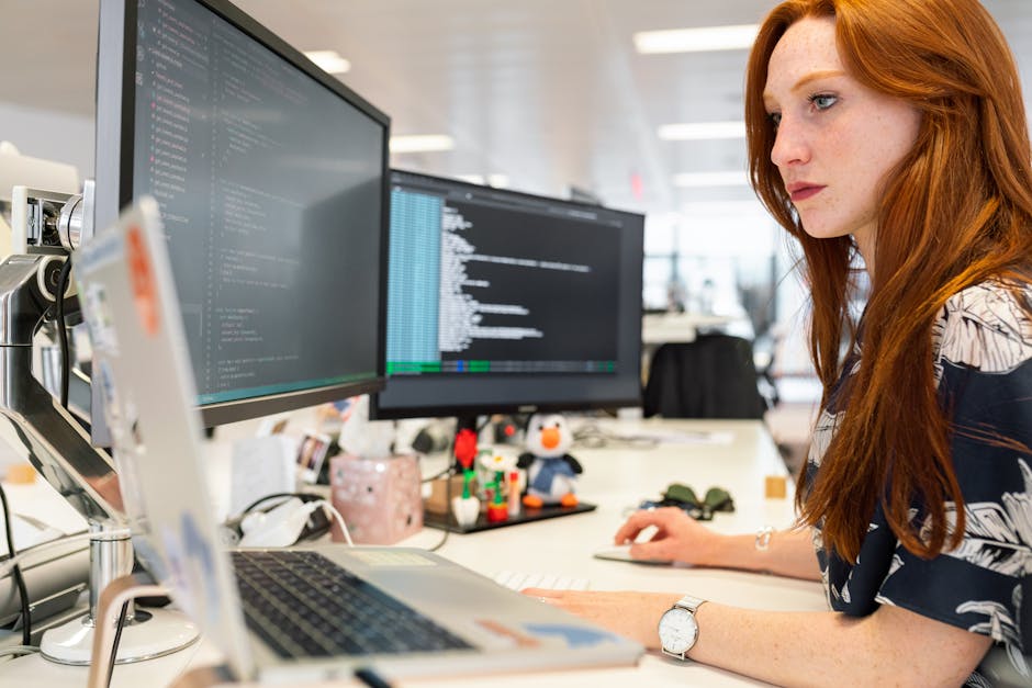 a woman sitting at a desk with two computer screens